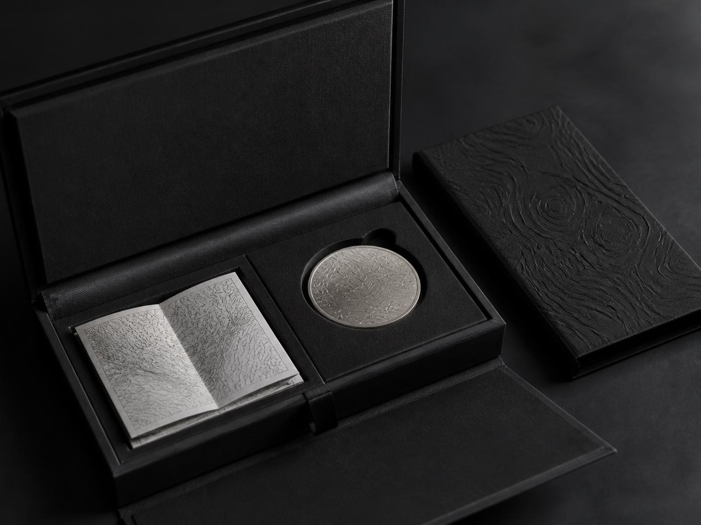 Open black linen collector case with folded chart and brushed titanium coin